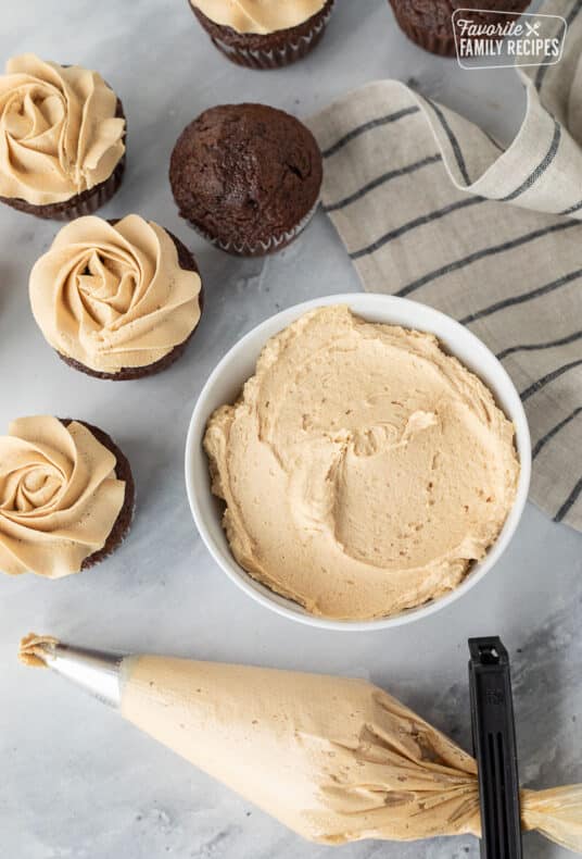 Bowl of Peanut Butter Frosting with a piping bag of Peanut Butter Frosting and chocolate cupcakes.