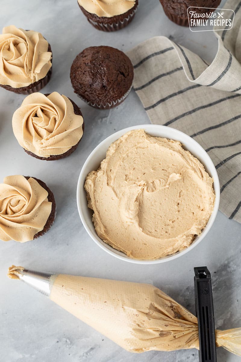 Bowl of Peanut Butter Frosting with a piping bag of Peanut Butter Frosting and chocolate cupcakes.