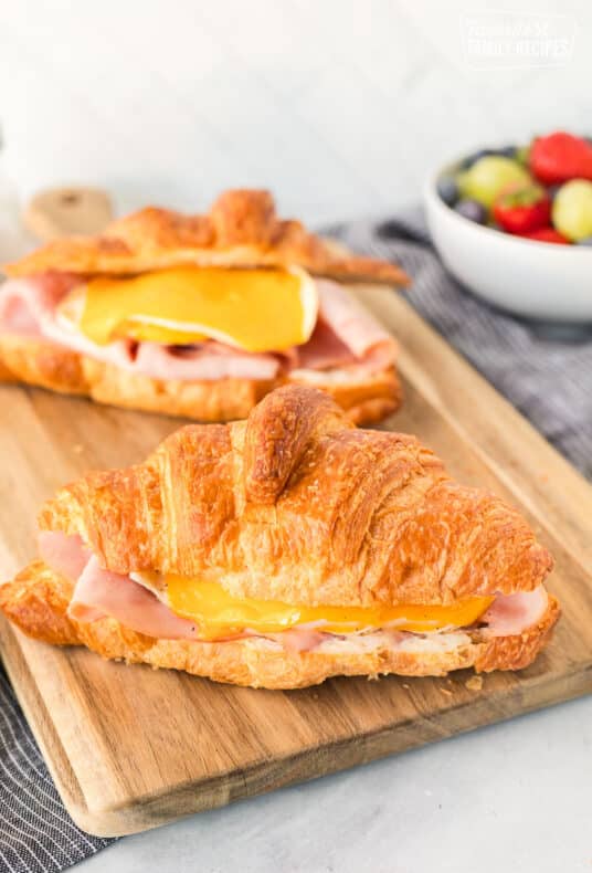 Cutting board with two Croissant Breakfast Sandwiches.