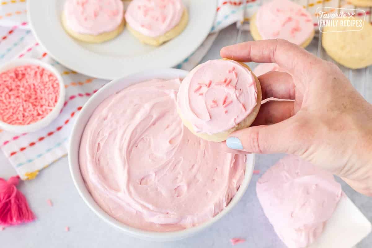 Hand holding a sugar cookie frosted with pink sugar cookie frosting and pink sprinkles.