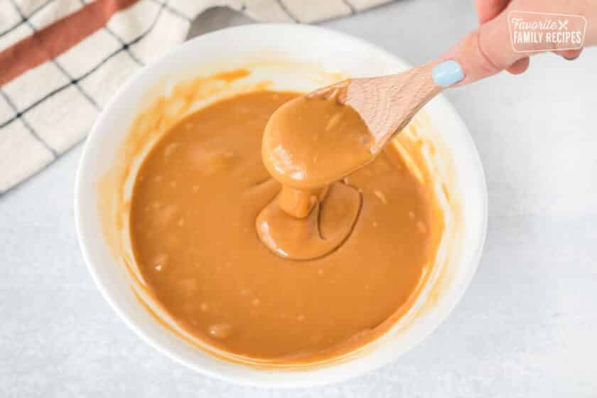 Bowl of melted caramels and a wooden spoon drizzling the caramel.