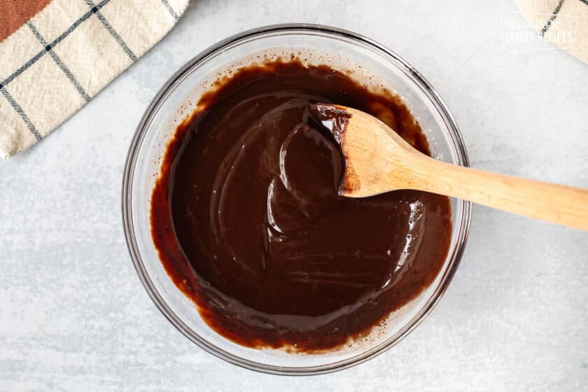 Mixing bowl of chocolate ganache with wooden spoon.