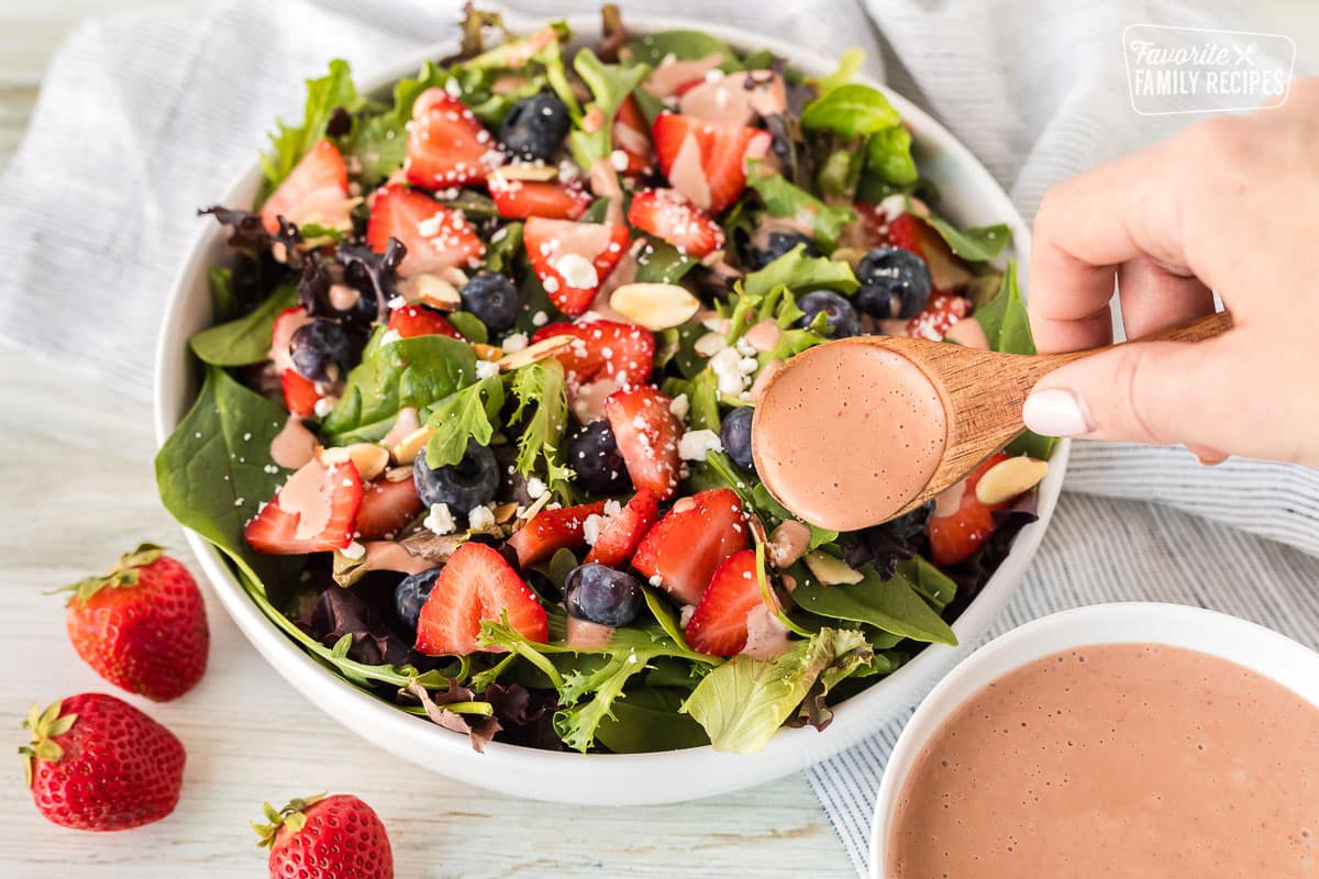 Pouring a spoon full of Strawberry Vinaigrette on a salad.