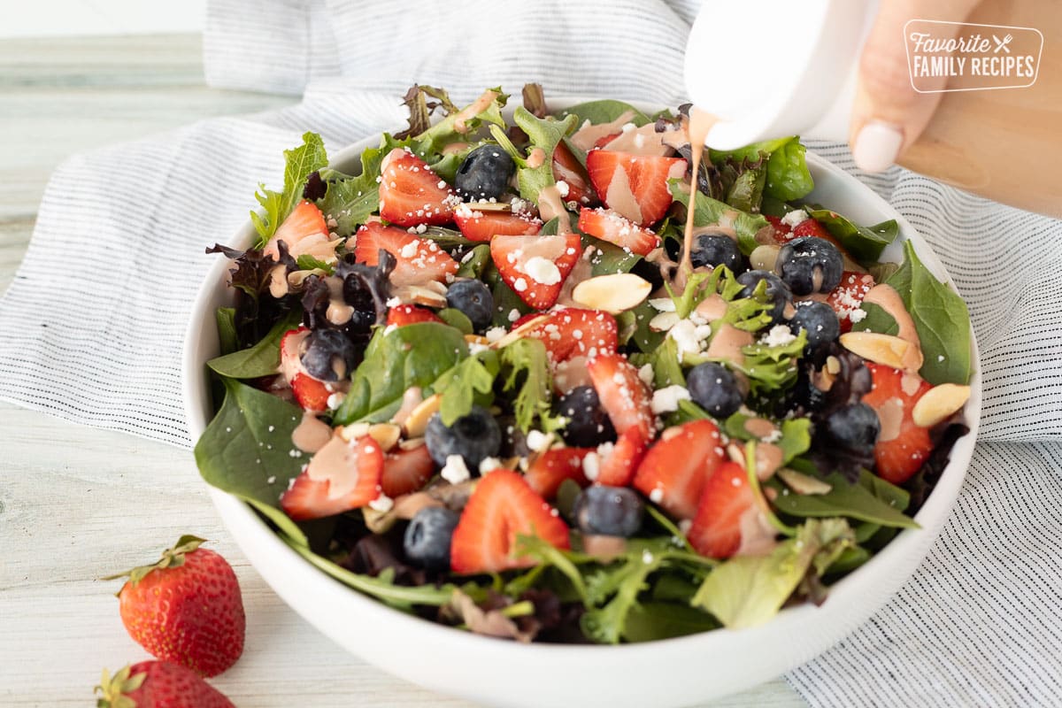 Pouring Strawberry Vinaigrette onto green salad.