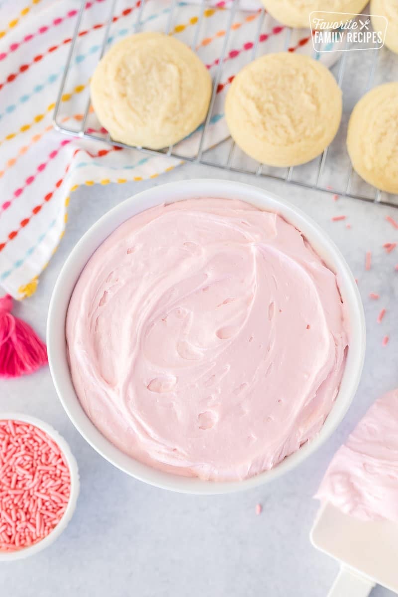 Bowl of pink Sugar Cookie Frosting next to cookies.