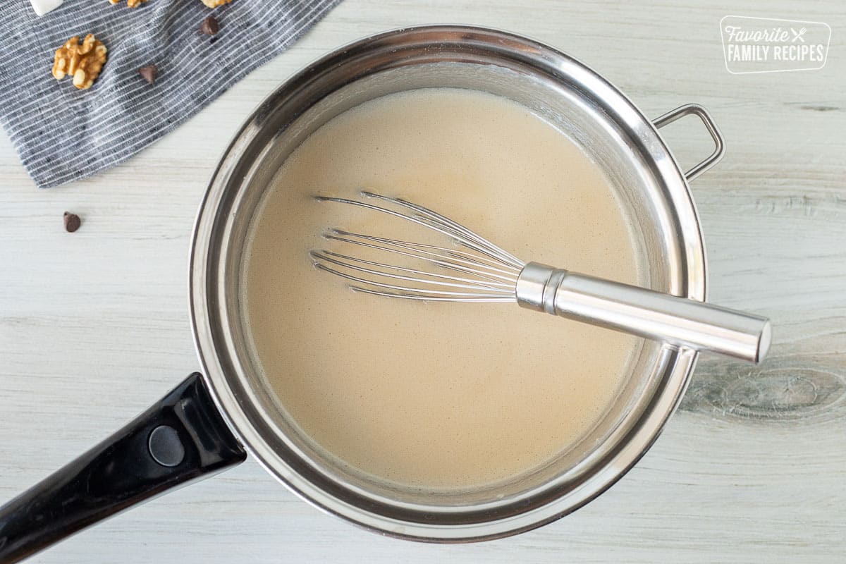 Pan of boiled hot evaporated milk and sugar with a whisk.