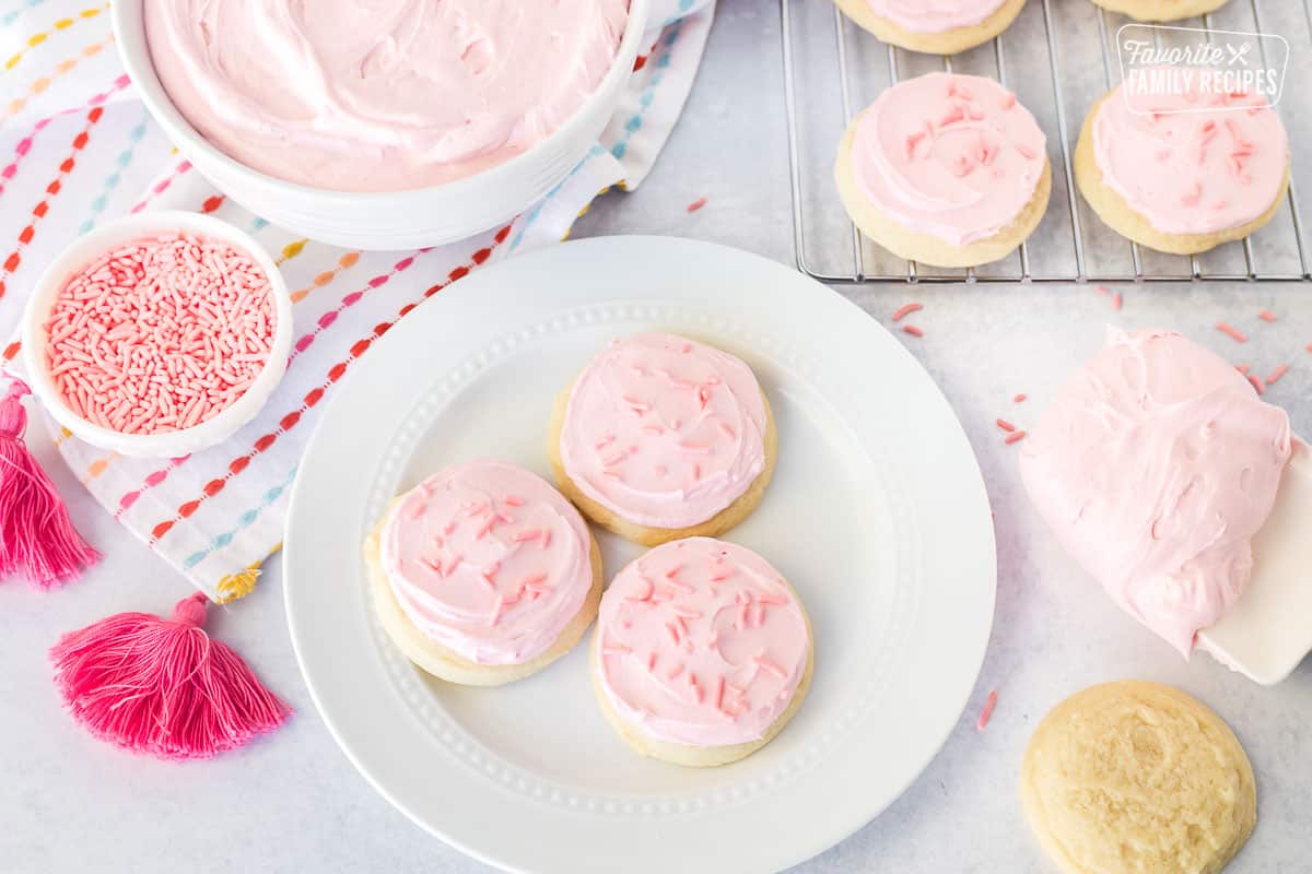 Plate of three sugar cookies decorated with pink sugar cookie frosting and pink sprinkles.