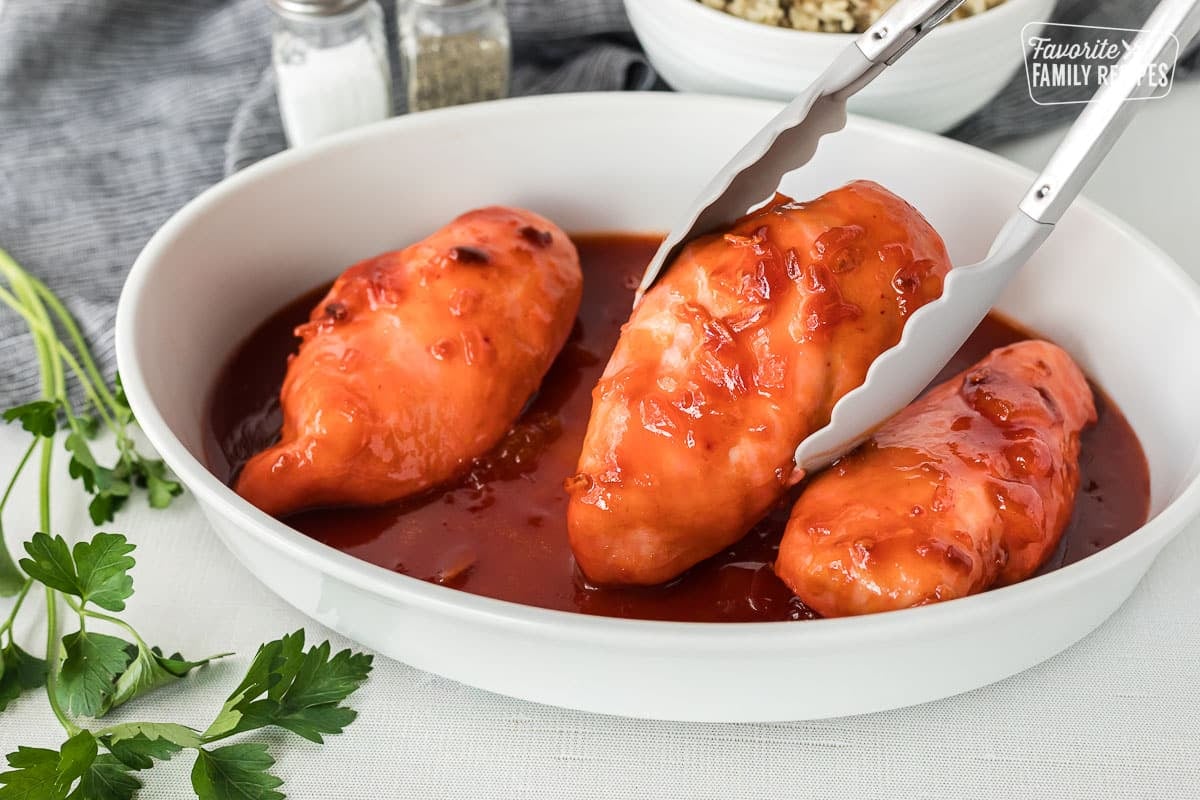 Tongs grabbing Apricot Chicken breast from a baking dish.