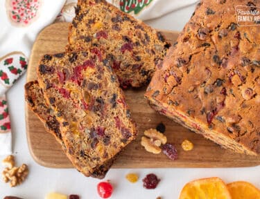 Three slices of Fruit Cake stacked together on a cutting board next to a loaf of Fruit Cake.