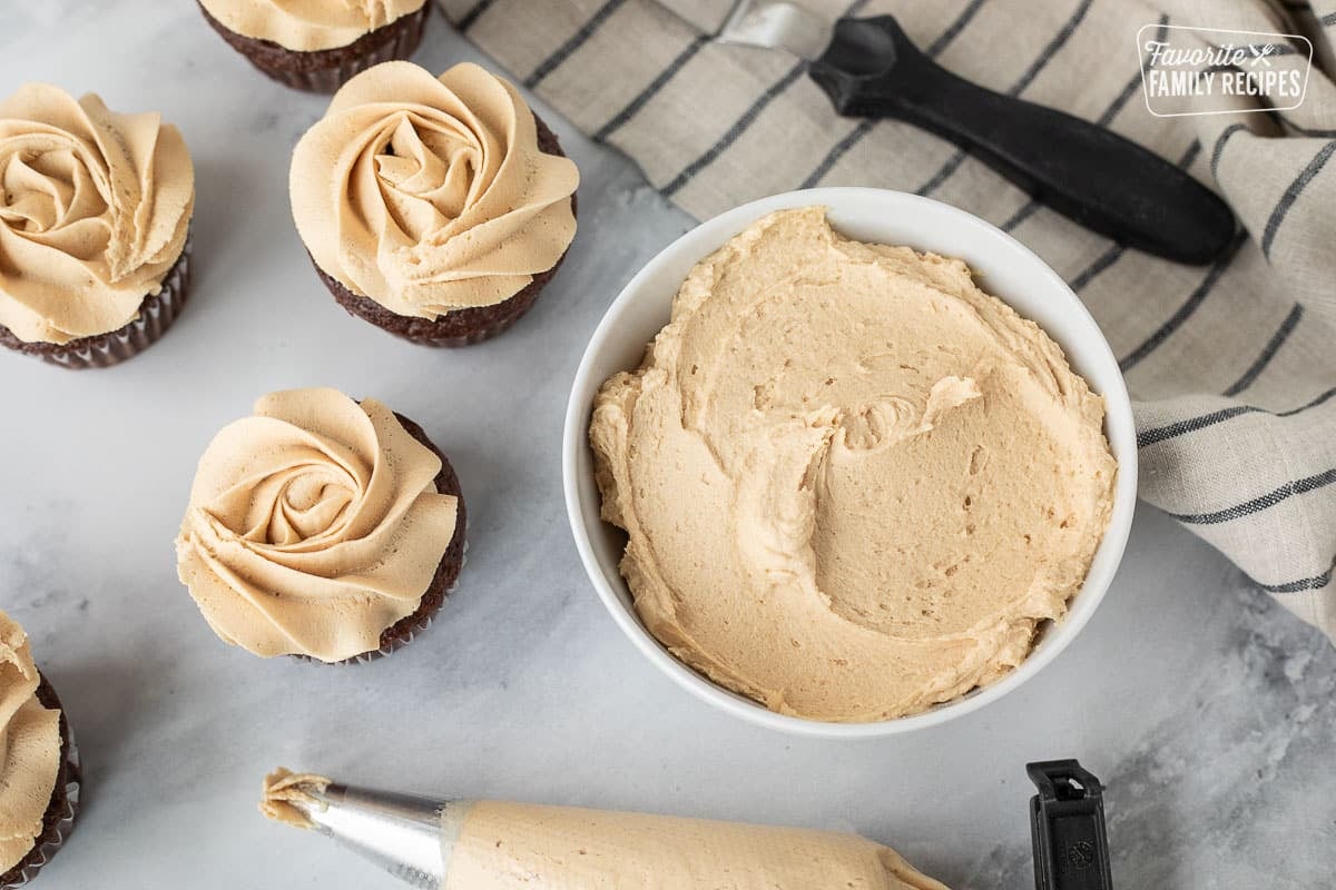 Bowl of Peanut Butter frosting next to decorated cupcakes and piping bag.