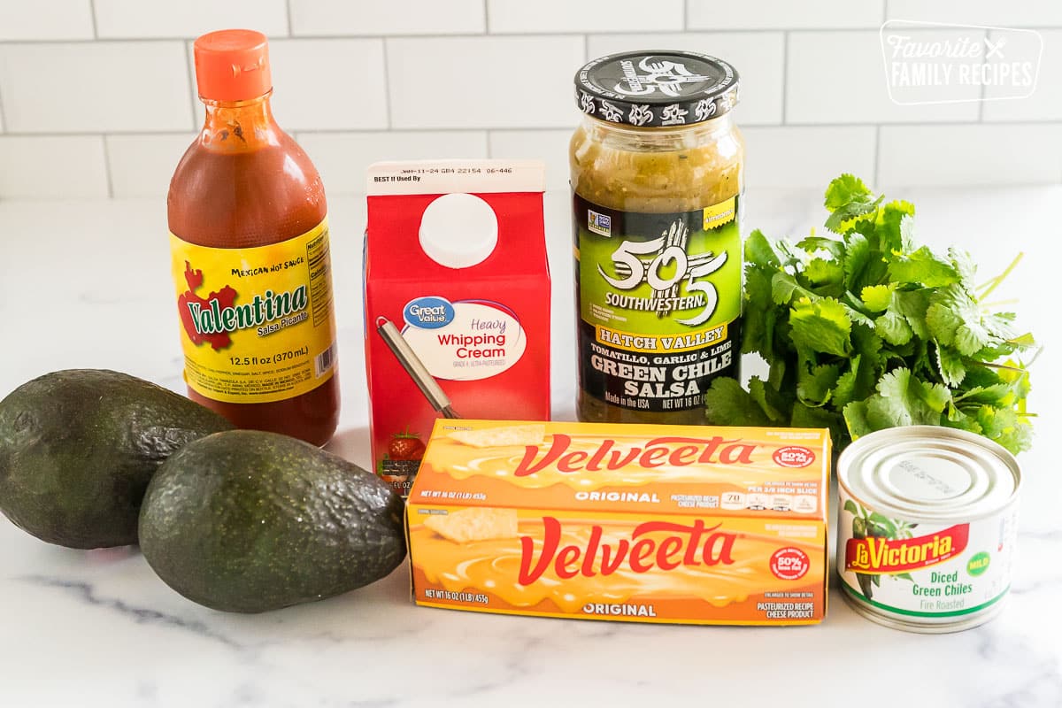 avocados, hot sauce, velveeta, salsa verde, cilantro, and a can of green chiles on a countertop