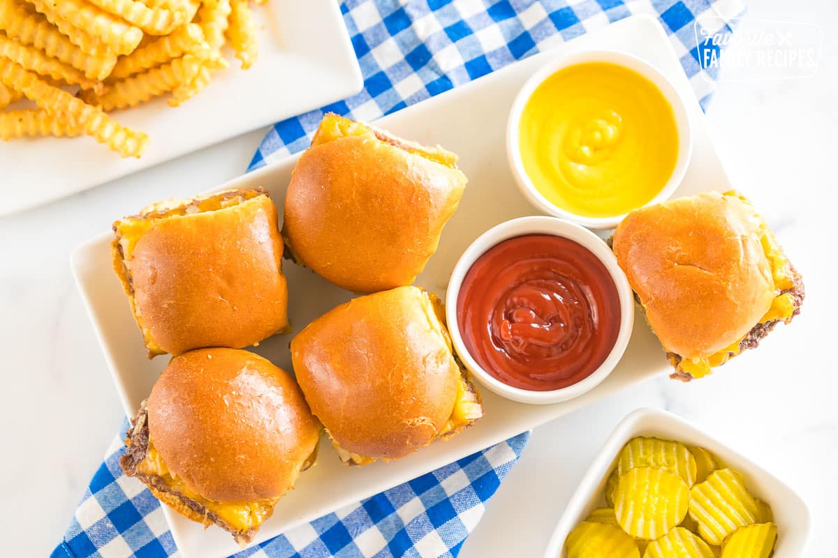 Mini burgers on a platter with bowls of ketchup and mustard