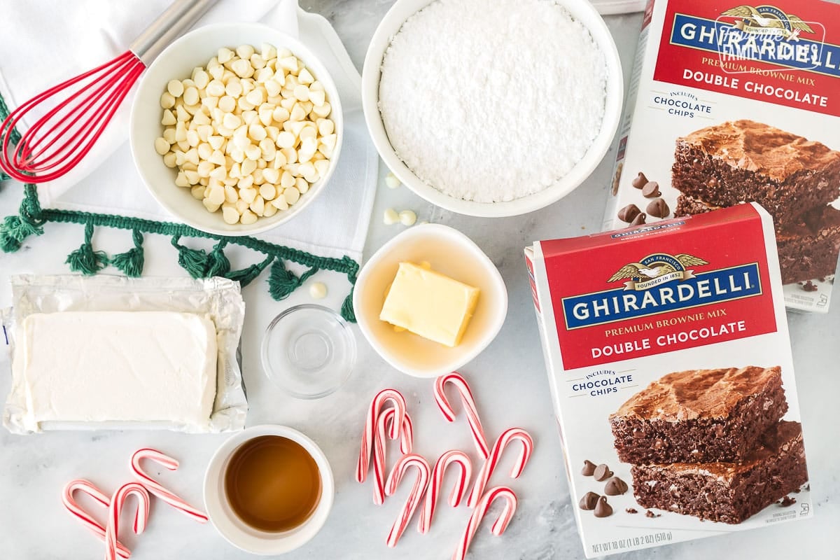 Ingredients to make White Chocolate Peppermint Brownies including white chocolate chips, powdered sugar, brownie mix, butter, vanilla, almond extract, cream cheese and candy canes.