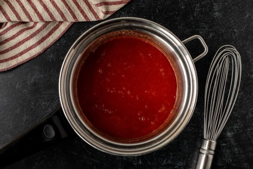 Pan with simmered Arby's red sauce with a whisk on the side.