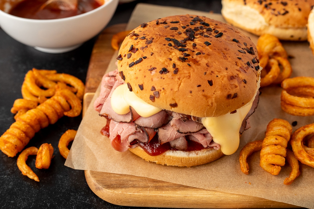 Top view of an Arby's Beef and Cheddar sandwich with an onion bun. Curly fries on the side.