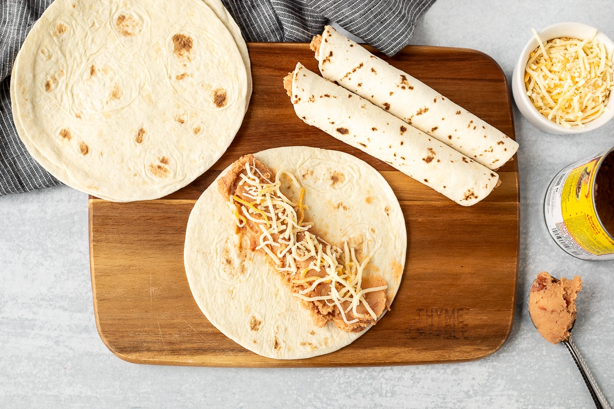 Cutting board with flour tortillas, refried beans and cheese on top.