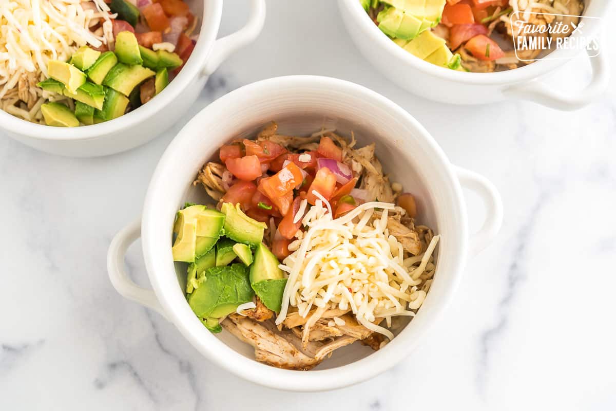 A white bowl with shredded chicken, avocado, cheese, and pico de gallo