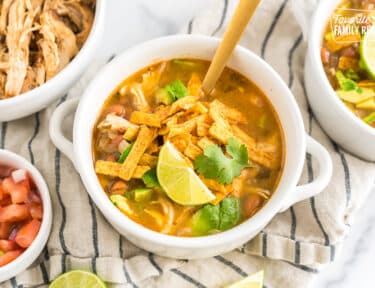 A bowl of cafe rio chicken tortilla soup topped with tortilla chips, cilantro, and lime wedges