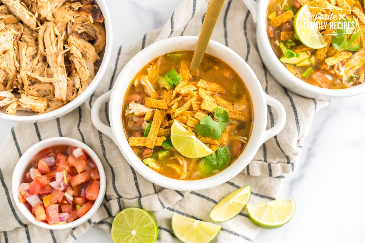 A bowl of cafe rio chicken tortilla soup topped with tortilla chips, cilantro, and lime wedges