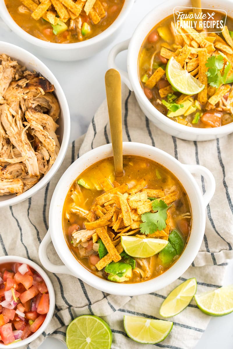 A bowl of cafe rio chicken tortilla soup topped with tortilla chips, cilantro, and lime wedges