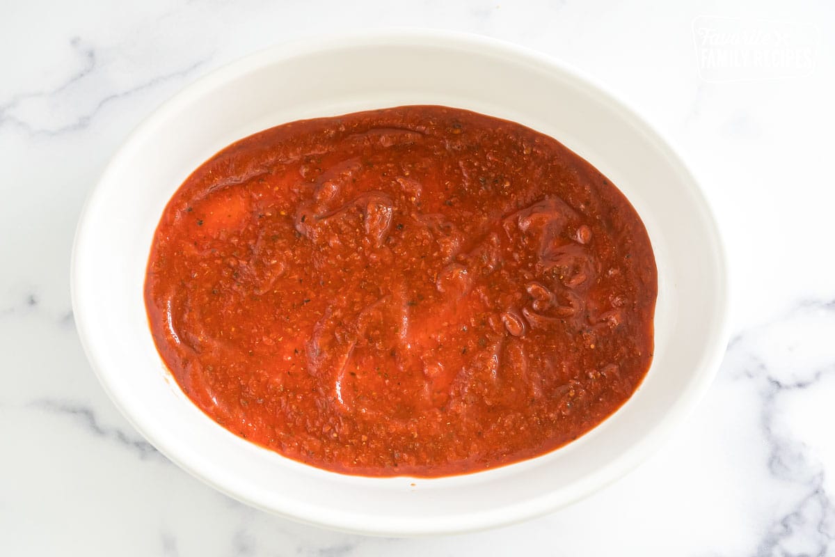 A baking dish with a layer of marinara sauce on the bottom.