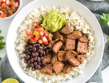 A bowl of cilantro lime rice topped with meat, beans, pico, and guac