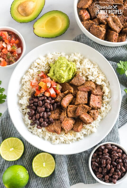 A bowl of cilantro lime rice topped with meat, beans, pico, and guac