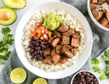 A bowl of cilantro lime rice topped with meat, beans, pico, and guac