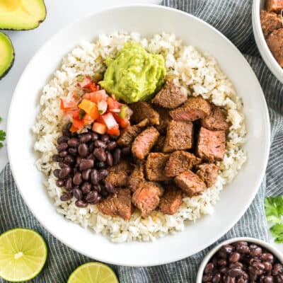 A bowl of cilantro lime rice topped with meat, beans, pico, and guac