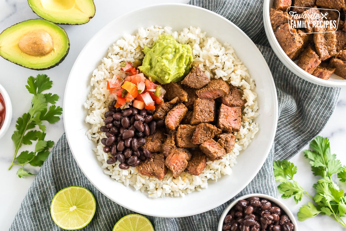 A bowl of cilantro lime rice topped with meat, beans, pico, and guac