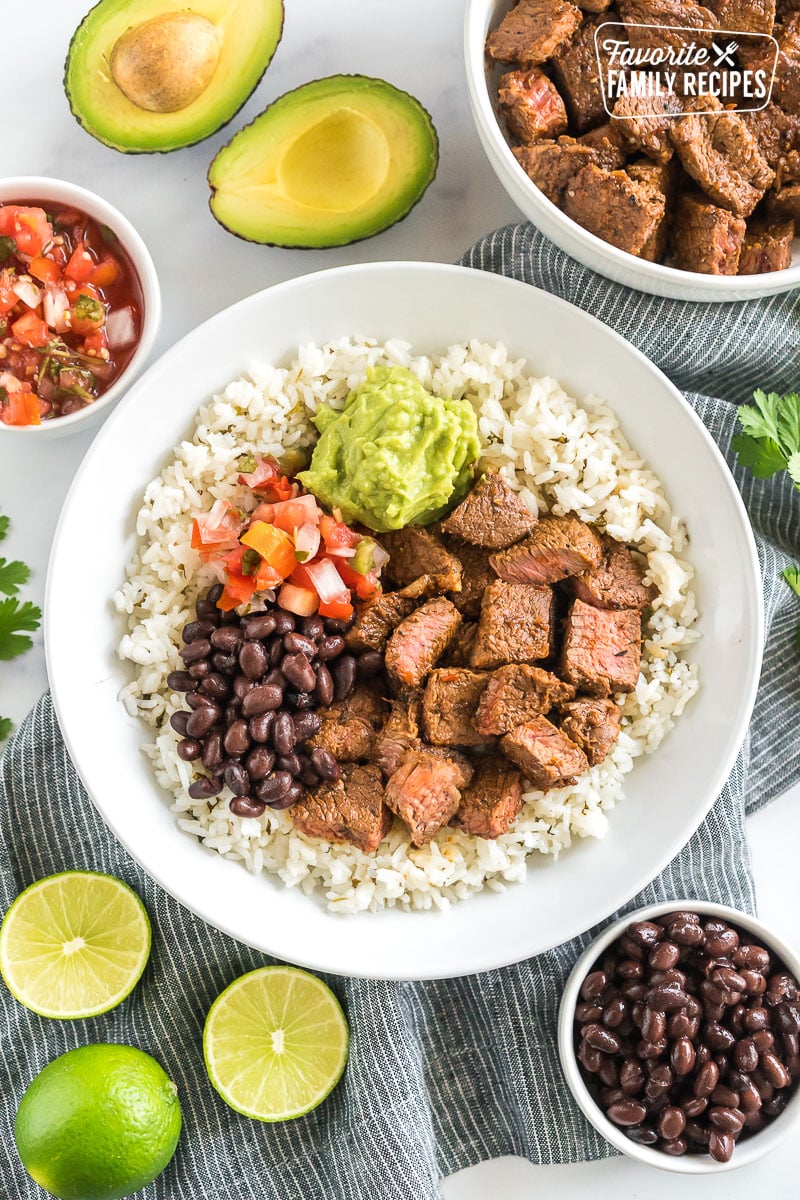 A bowl of cilantro lime rice topped with meat, beans, pico, and guac