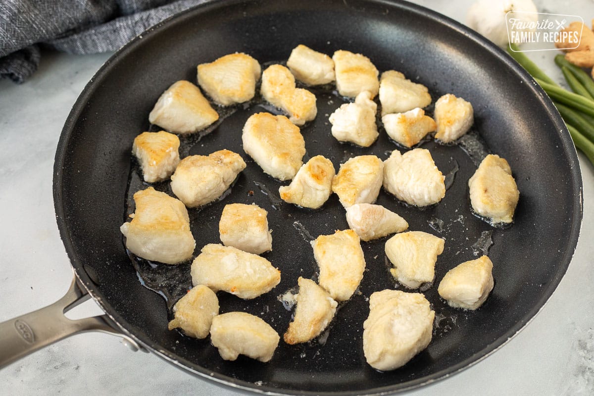 Skillet with cut up pieces of chicken cooking.