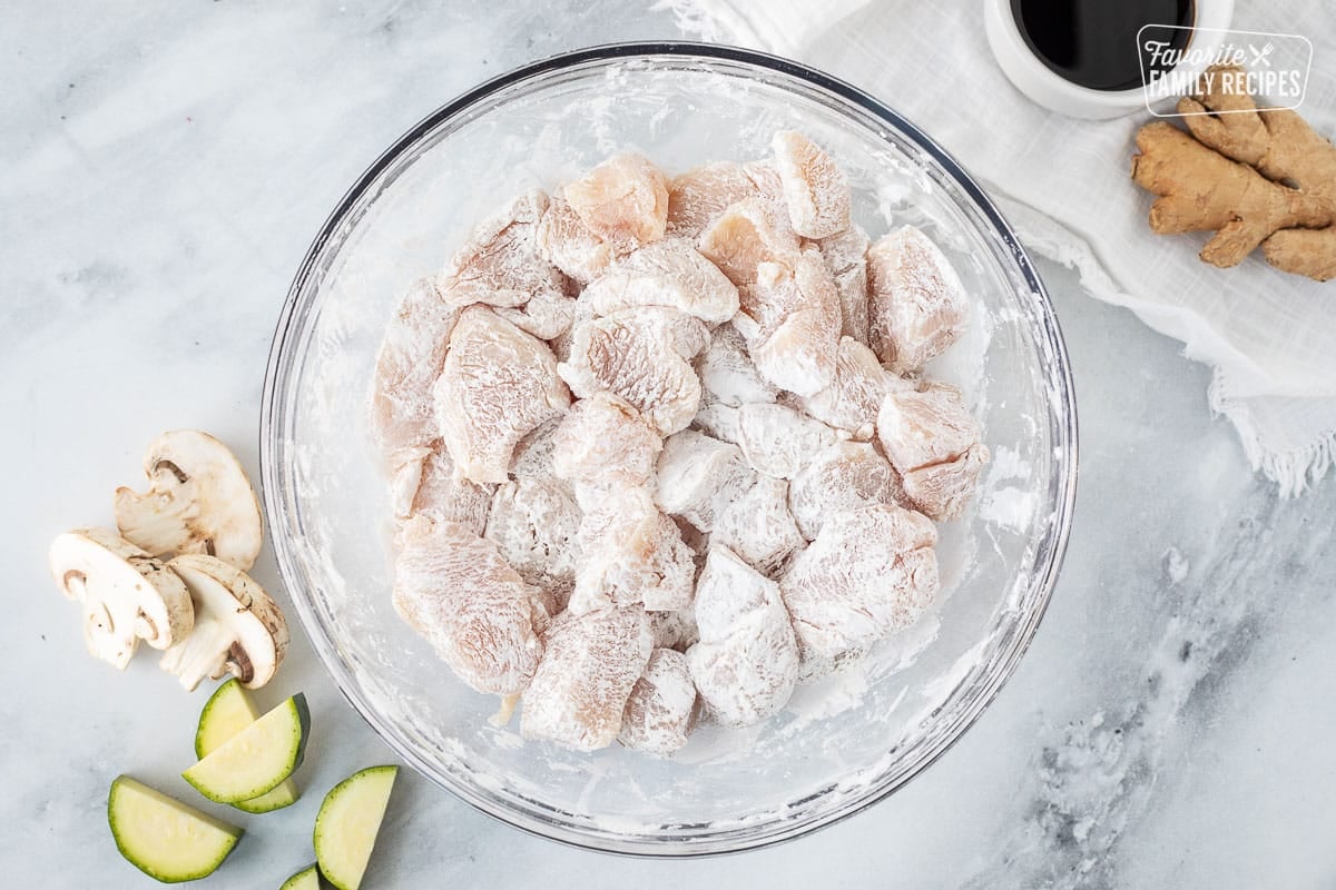 Bowl of cut up pieces of chicken coated with corn starch.