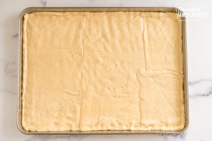 Crescent rolls pressed together and formed into a rectangular pizza crust on a baking sheet