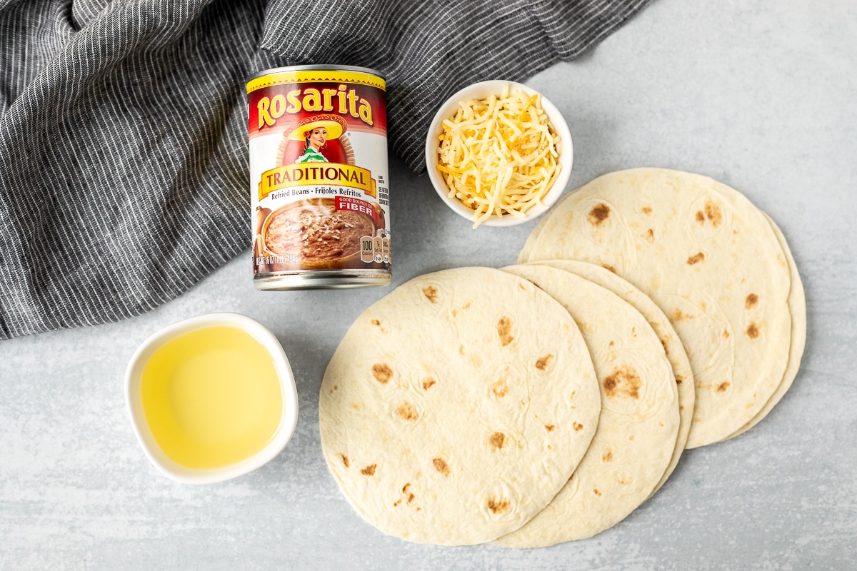Ingredients to make Crisp Bean Burritos including flour tortillas, refried beans, cheese and oil.