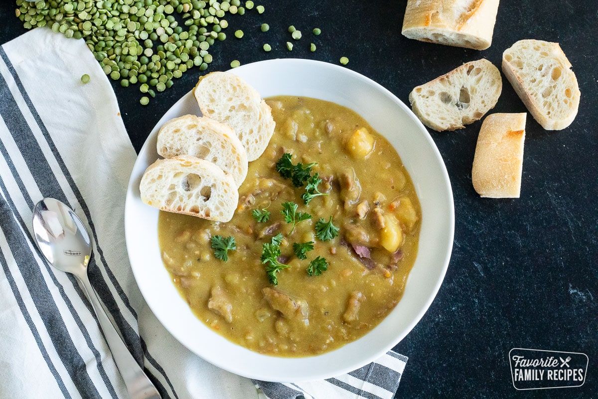 Split pea soup in a bowl next to a spoon and bread slices.