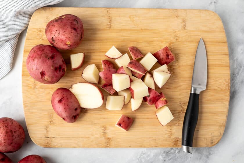 Cutting board with cut red potatoes and a knife.