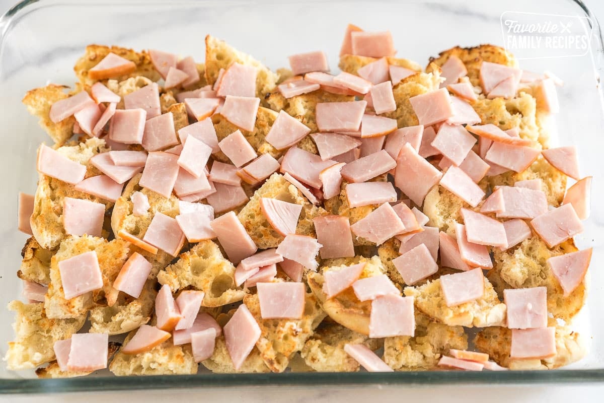 toasted and buttered english muffins topped with sliced canadian bacon in a baking dish