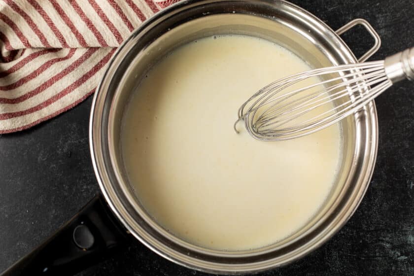 Pan with creamy sauce and a whisk.