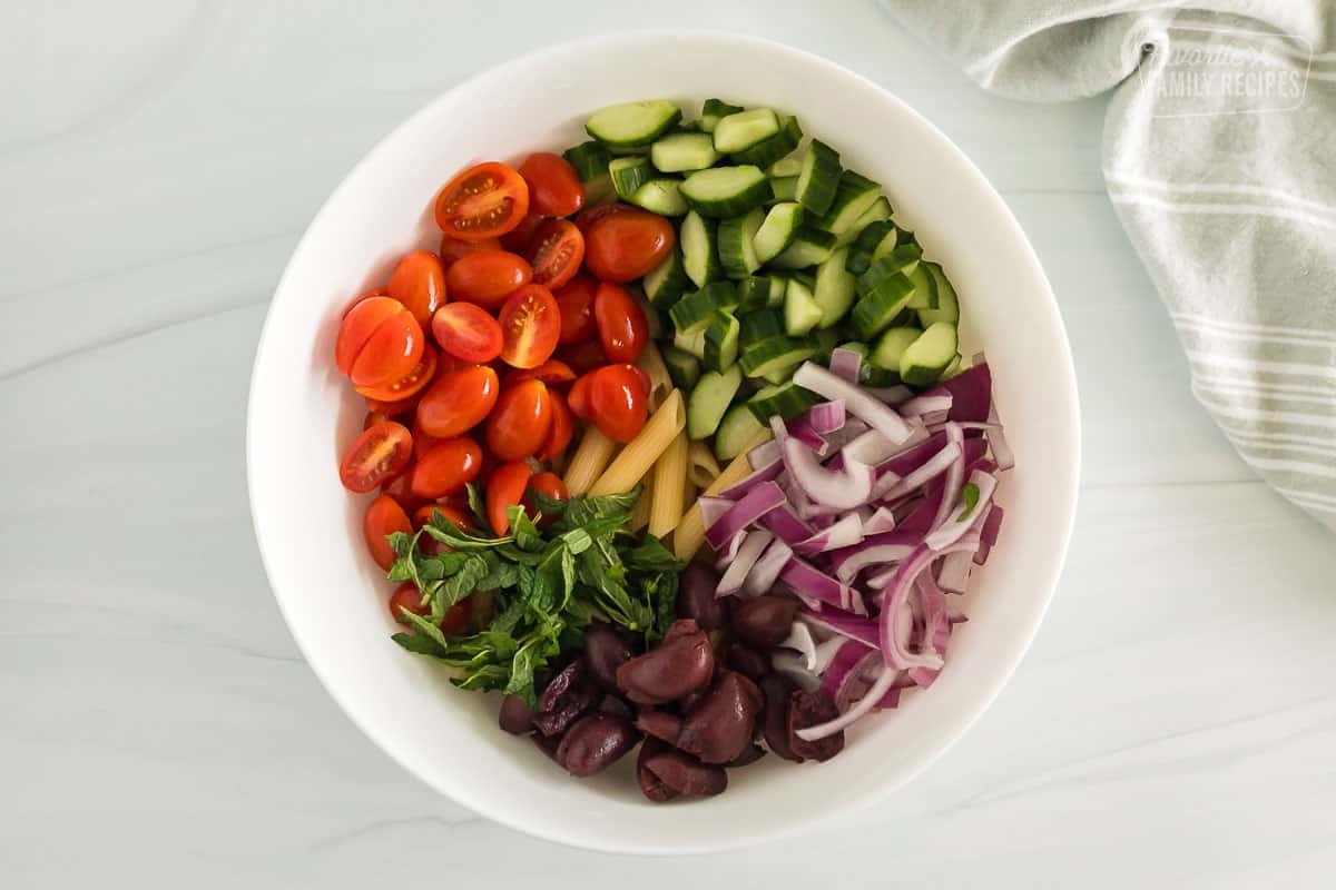 penne pasta, onions, kalamata olives, mint, cherry tomatoes, and cucumbers inside a bowl to be mixed together