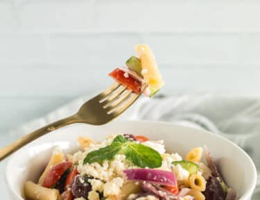 greek pasta salad in a bowl and a fork with a bite of the salad on it