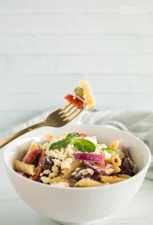 greek pasta salad in a bowl and a fork with a bite of the salad on it