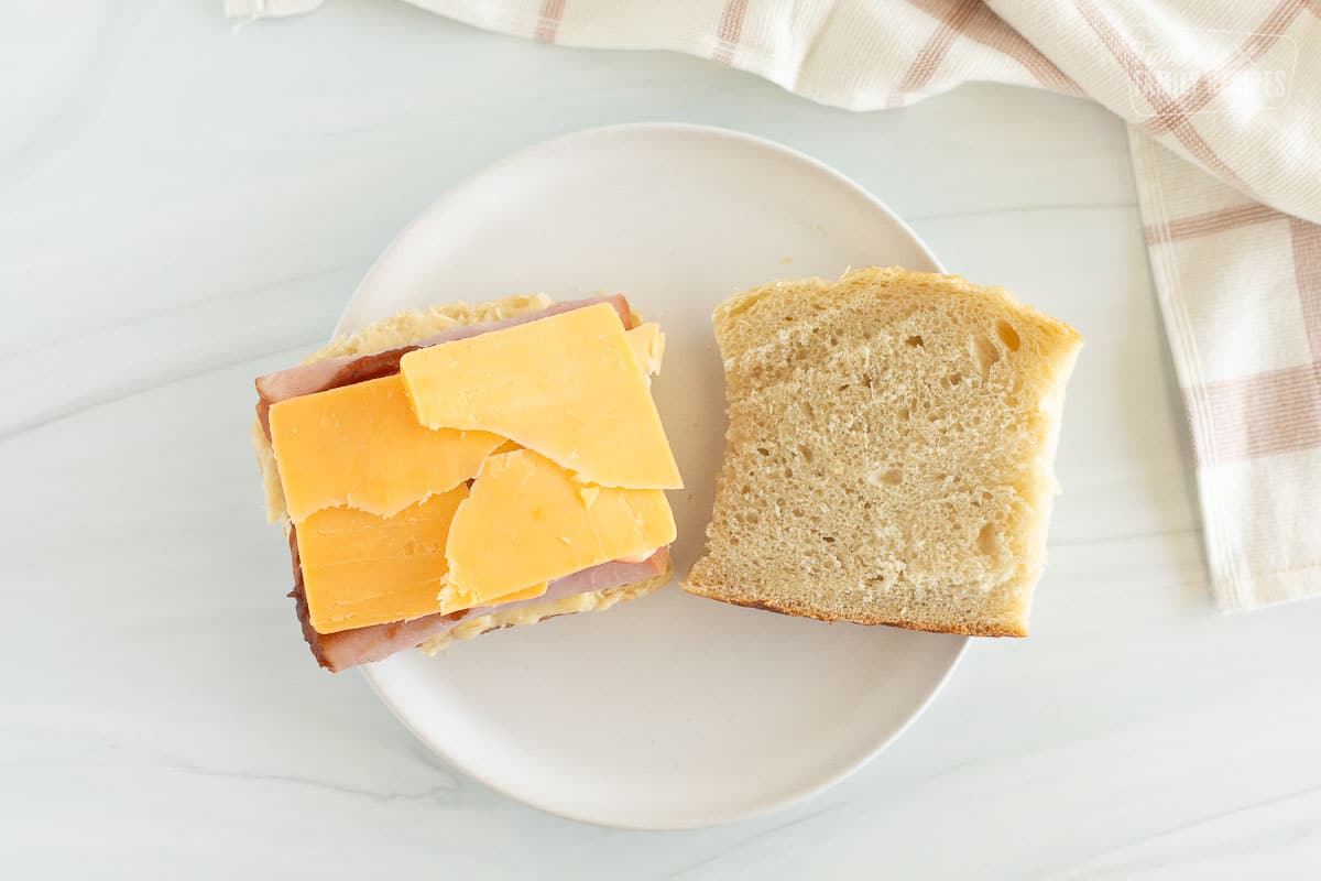 A grilled ham and cheese being assembled with layers of ham, sharp cheddar, butter, brie cheese, apple slices, and apple butter