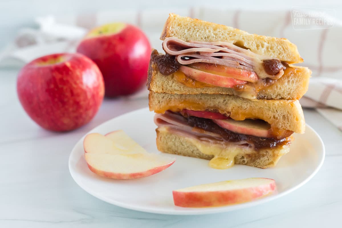 Halves of a grilled ham and cheese stacked on top of each other with apples on the side