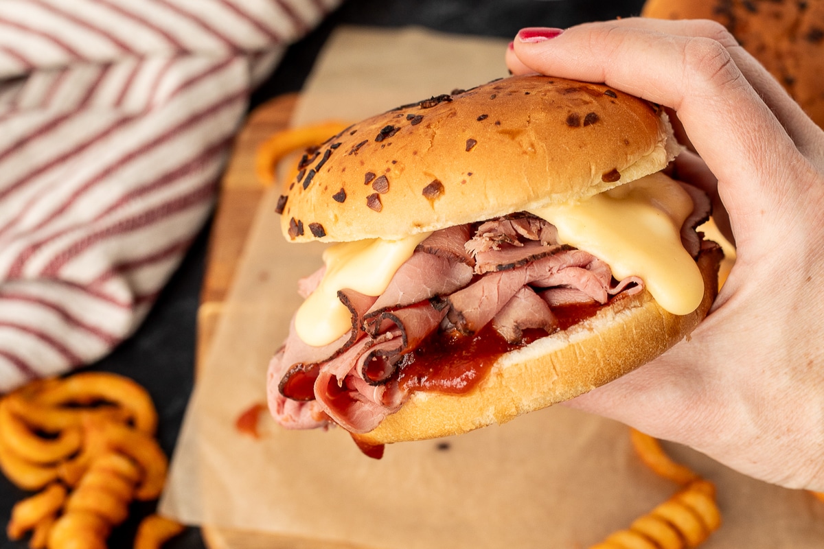 Hand holding a Beef and Cheddar sandwich.