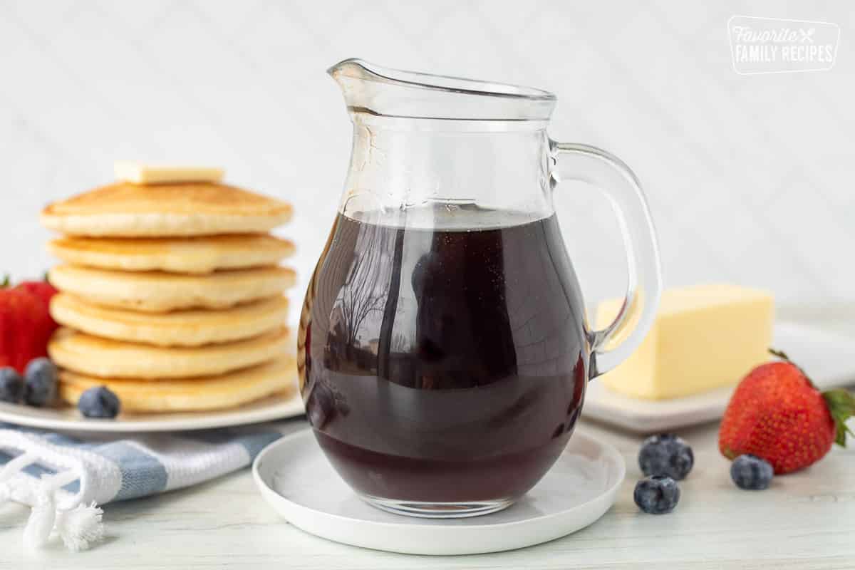 Jar of Homemade Maple Syrup next to a stack of pancakes, butter and berries.
