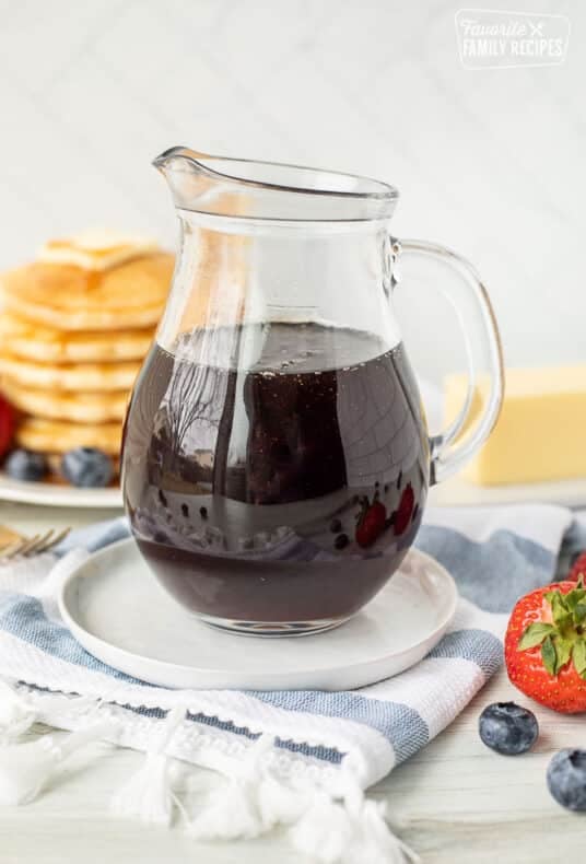 Jar of homemade maple syrup in front of a stack of pancakes and butter.