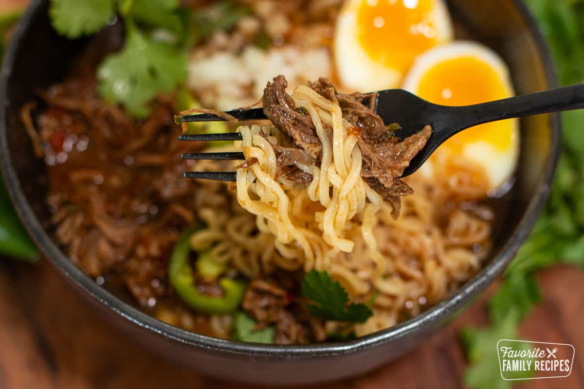 A fork holding a bite of birria ramen with noodles