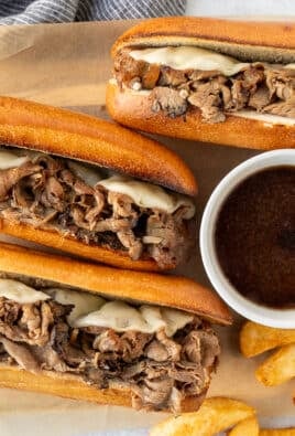 Three French Dip Sandwiches with toasted French bread, sliced roast beef and melted provolone cheese. Bowl of au jus and French fries on the side.