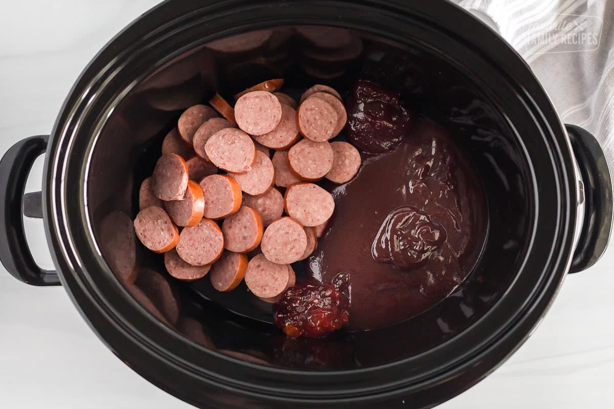 Slices of Kielbasa barbecue sauce, jalapeno jelly and strawberry jam all inside of a crockpot.